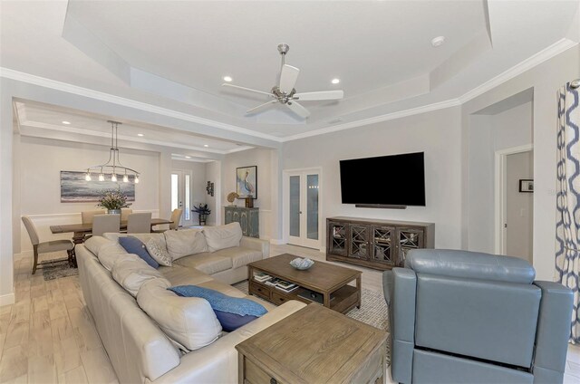 living room with french doors, a tray ceiling, ceiling fan, ornamental molding, and light hardwood / wood-style flooring