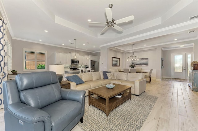 living room with ornamental molding, light hardwood / wood-style floors, and a raised ceiling