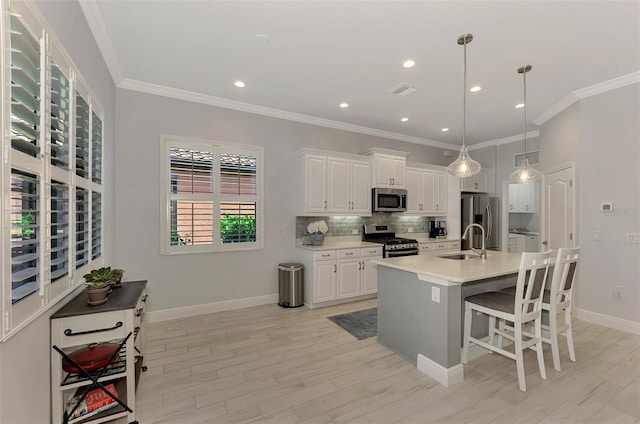 kitchen featuring an island with sink, appliances with stainless steel finishes, white cabinetry, sink, and decorative light fixtures