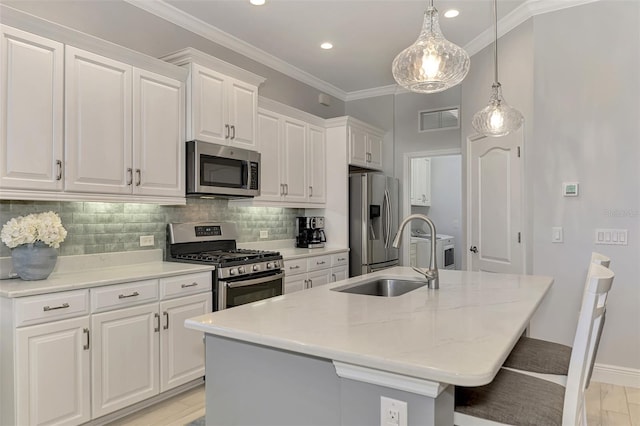 kitchen with appliances with stainless steel finishes, pendant lighting, white cabinets, and an island with sink