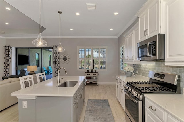 kitchen with stainless steel appliances, a center island with sink, sink, white cabinets, and light hardwood / wood-style floors