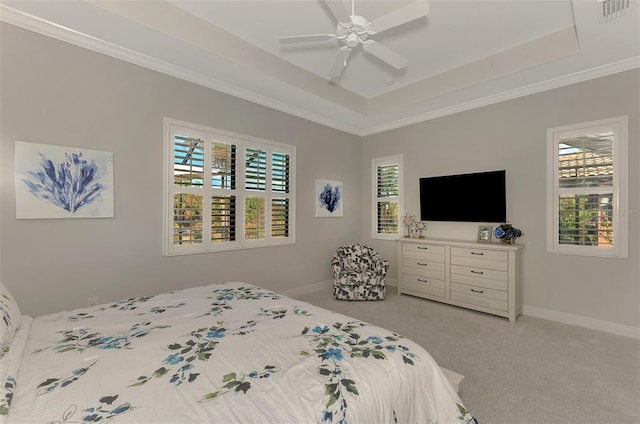 carpeted bedroom with ornamental molding, multiple windows, a tray ceiling, and ceiling fan