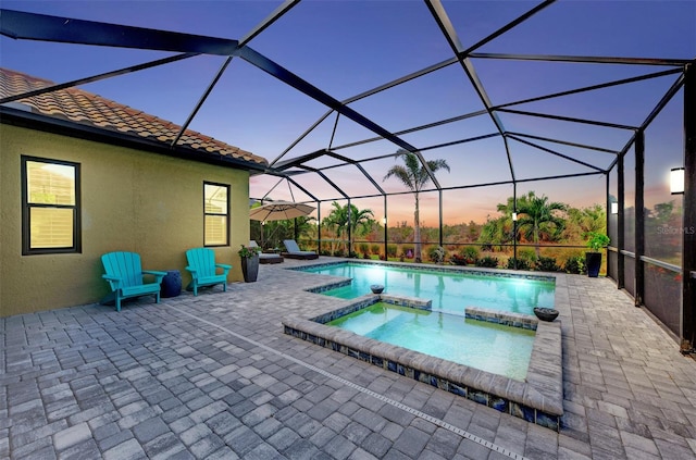 pool at dusk with an in ground hot tub, a patio area, and a lanai