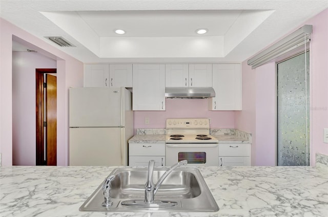 kitchen with white appliances, a tray ceiling, sink, and white cabinets