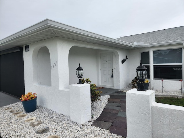 doorway to property featuring stucco siding and a shingled roof