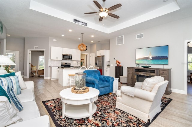 living room featuring a raised ceiling, light wood-type flooring, and plenty of natural light