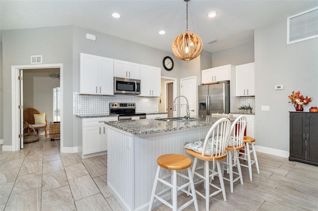 kitchen with appliances with stainless steel finishes, white cabinets, sink, and an island with sink