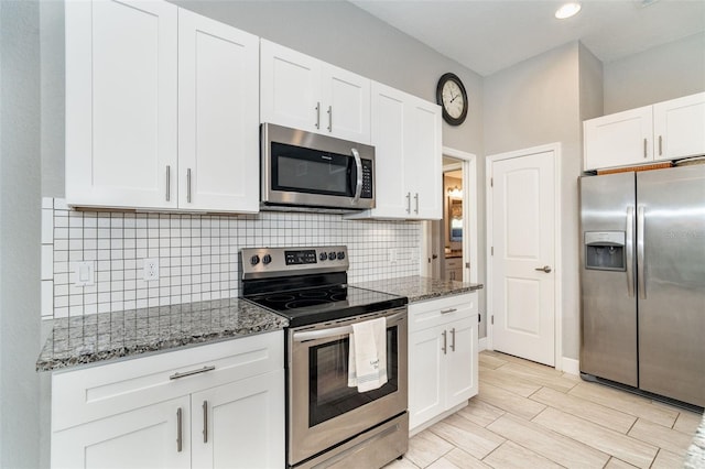 kitchen with backsplash, dark stone counters, light wood-type flooring, white cabinetry, and appliances with stainless steel finishes