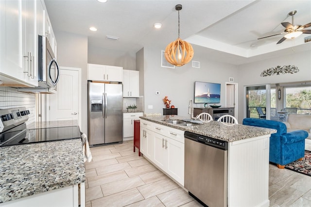 kitchen featuring light stone counters, an island with sink, appliances with stainless steel finishes, white cabinetry, and sink