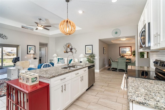 kitchen with hanging light fixtures, appliances with stainless steel finishes, white cabinetry, a kitchen island with sink, and sink