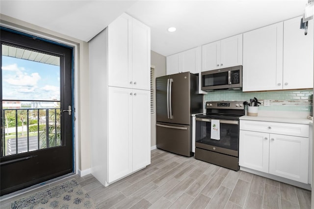 kitchen with backsplash, white cabinetry, stainless steel appliances, and light wood-type flooring