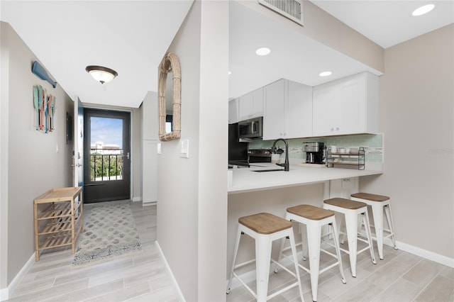 kitchen featuring kitchen peninsula, backsplash, a kitchen bar, light wood-type flooring, and white cabinets