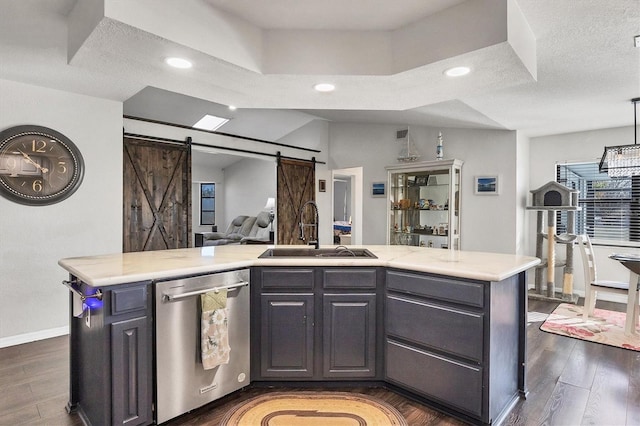 kitchen featuring sink, a barn door, dark hardwood / wood-style flooring, stainless steel dishwasher, and a kitchen island with sink