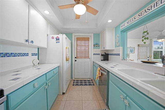 kitchen featuring light tile patterned floors, a tray ceiling, white cabinets, white fridge, and dishwasher