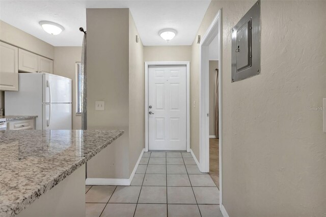 kitchen featuring white cabinets, electric panel, light tile patterned floors, light stone countertops, and white fridge