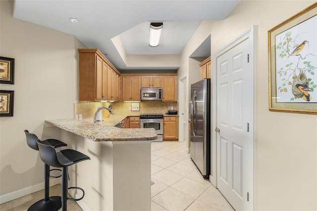 kitchen featuring a kitchen breakfast bar, kitchen peninsula, light stone countertops, appliances with stainless steel finishes, and tasteful backsplash