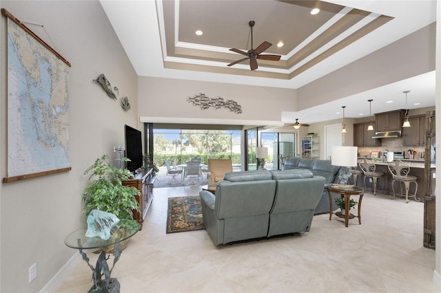 living room with a towering ceiling, ornamental molding, a raised ceiling, and ceiling fan