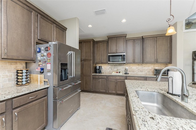 kitchen with hanging light fixtures, sink, appliances with stainless steel finishes, light stone counters, and tasteful backsplash