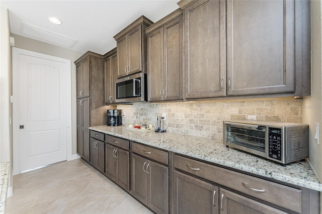 kitchen featuring light stone countertops, tasteful backsplash, dark brown cabinetry, and light tile patterned flooring