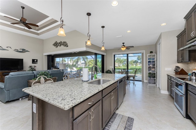 kitchen featuring ceiling fan, appliances with stainless steel finishes, an island with sink, light stone countertops, and sink