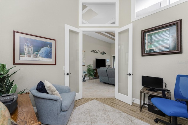 office area with french doors, light hardwood / wood-style floors, and a high ceiling