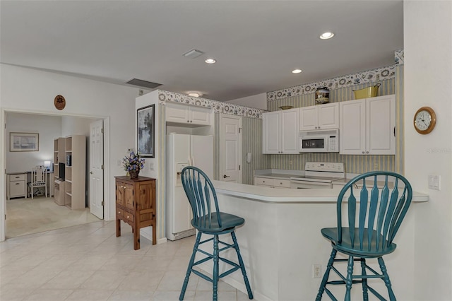 kitchen featuring white appliances, a breakfast bar area, kitchen peninsula, and white cabinets