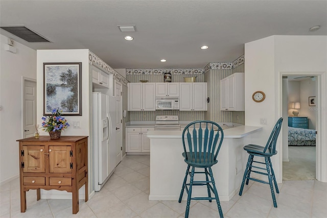 kitchen featuring a breakfast bar area, kitchen peninsula, white cabinetry, and white appliances