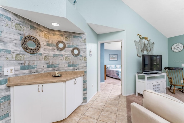 kitchen with wooden walls, light tile patterned floors, white cabinetry, and lofted ceiling