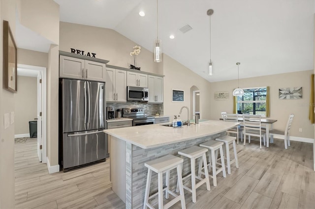 kitchen with a center island with sink, appliances with stainless steel finishes, pendant lighting, gray cabinetry, and sink