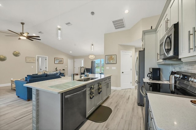 kitchen with appliances with stainless steel finishes, sink, lofted ceiling, pendant lighting, and a center island with sink