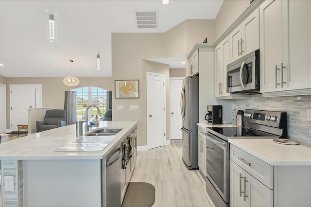 kitchen with sink, an island with sink, stainless steel appliances, decorative light fixtures, and decorative backsplash