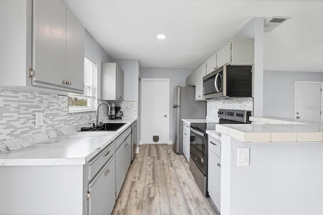 kitchen with light wood-type flooring, appliances with stainless steel finishes, gray cabinets, decorative backsplash, and sink