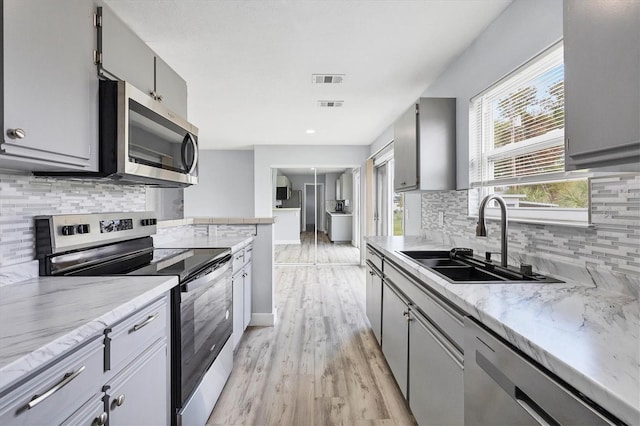 kitchen featuring light hardwood / wood-style floors, stainless steel appliances, decorative backsplash, sink, and gray cabinets