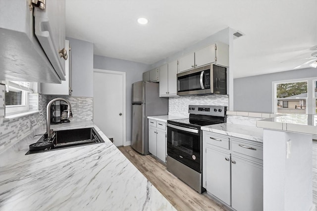 kitchen with stainless steel appliances, light wood-type flooring, decorative backsplash, sink, and ceiling fan