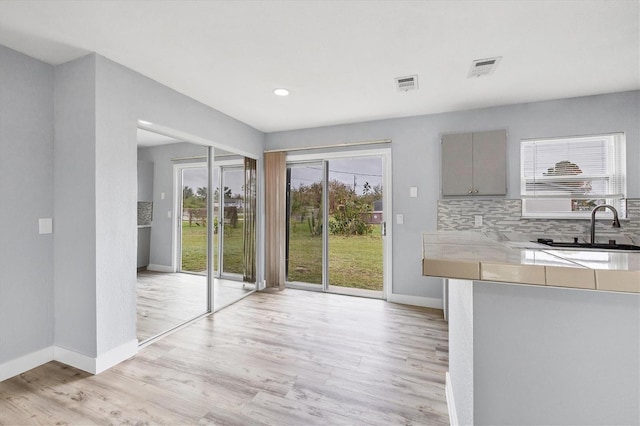 kitchen with gray cabinets, tasteful backsplash, sink, and light hardwood / wood-style floors