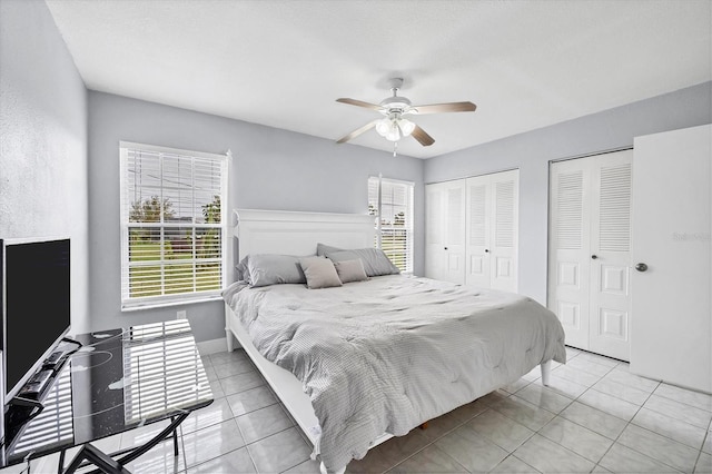 bedroom featuring light tile patterned floors, ceiling fan, and two closets