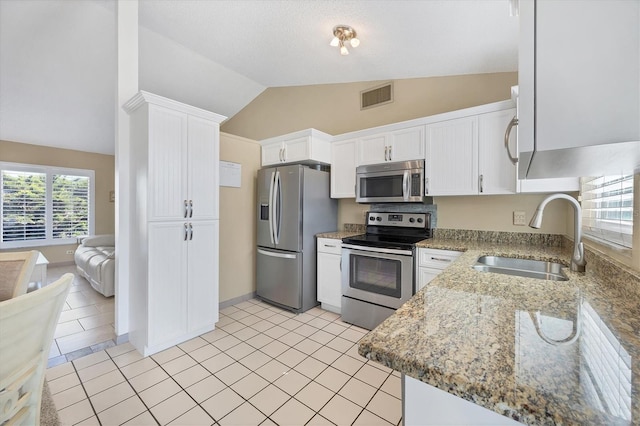 kitchen featuring light stone countertops, sink, stainless steel appliances, vaulted ceiling, and white cabinets