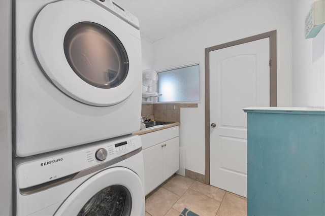 clothes washing area featuring sink, cabinets, light tile patterned floors, and stacked washer and dryer