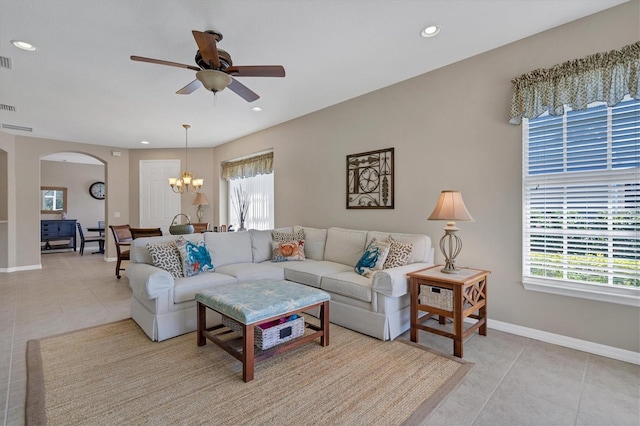 tiled living room with ceiling fan with notable chandelier