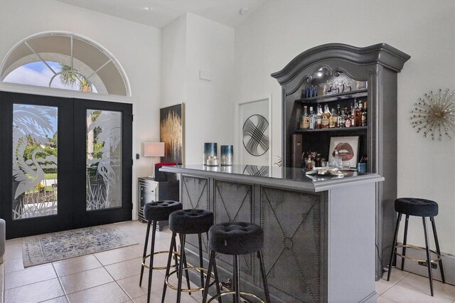 bar with light tile patterned floors, high vaulted ceiling, and french doors