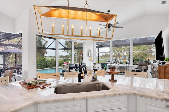 kitchen featuring hanging light fixtures, light stone countertops, sink, and white cabinets