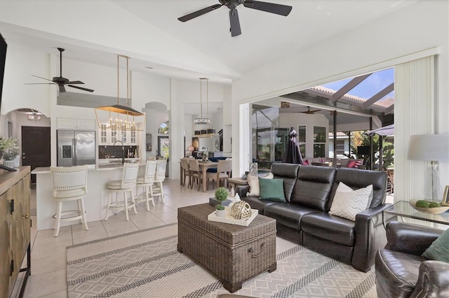 tiled living room featuring high vaulted ceiling, sink, and ceiling fan with notable chandelier