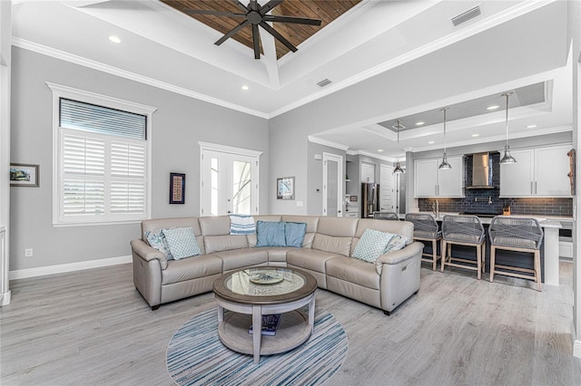 living room featuring ceiling fan, a raised ceiling, ornamental molding, and light wood-type flooring