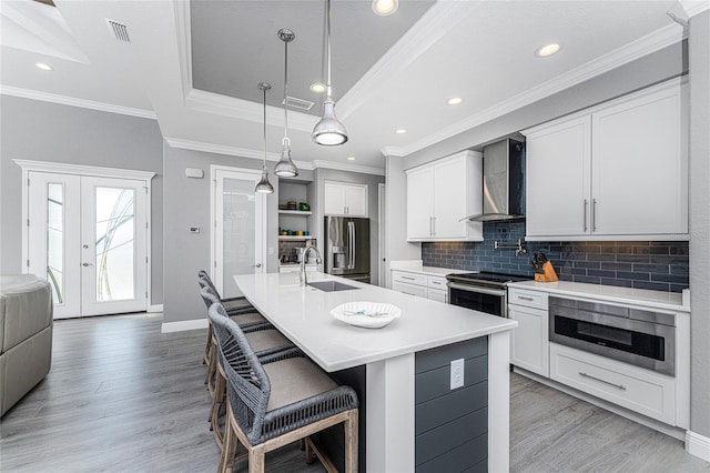 kitchen with white cabinetry, wall chimney range hood, appliances with stainless steel finishes, and a center island with sink