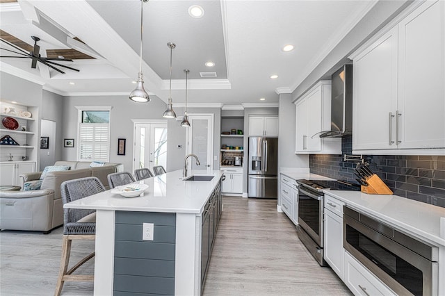 kitchen featuring wall chimney range hood, sink, hanging light fixtures, stainless steel appliances, and a breakfast bar