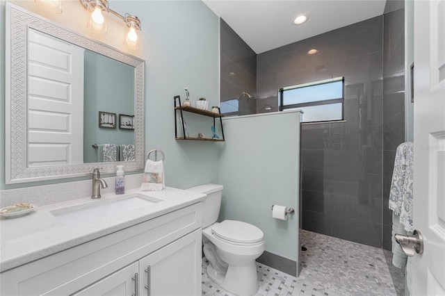 bathroom featuring vanity, a tile shower, and toilet