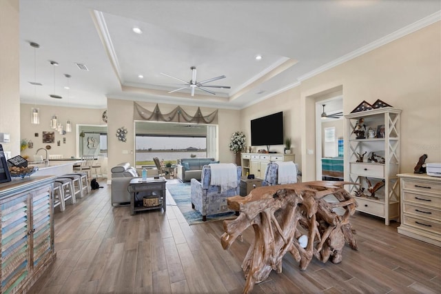 living room featuring ornamental molding, sink, hardwood / wood-style flooring, and a raised ceiling