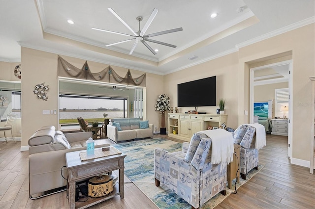 living room featuring crown molding, light hardwood / wood-style flooring, a raised ceiling, and ceiling fan