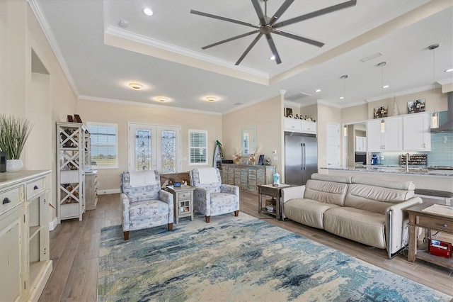 living room with ornamental molding, light hardwood / wood-style flooring, a tray ceiling, and ceiling fan