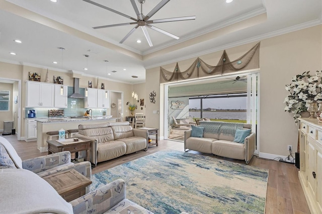 living room with light hardwood / wood-style floors, ornamental molding, a tray ceiling, and ceiling fan